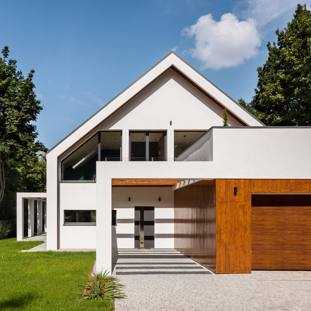 A white house with a wooden garage door and a paved driveway in a suburban setting.