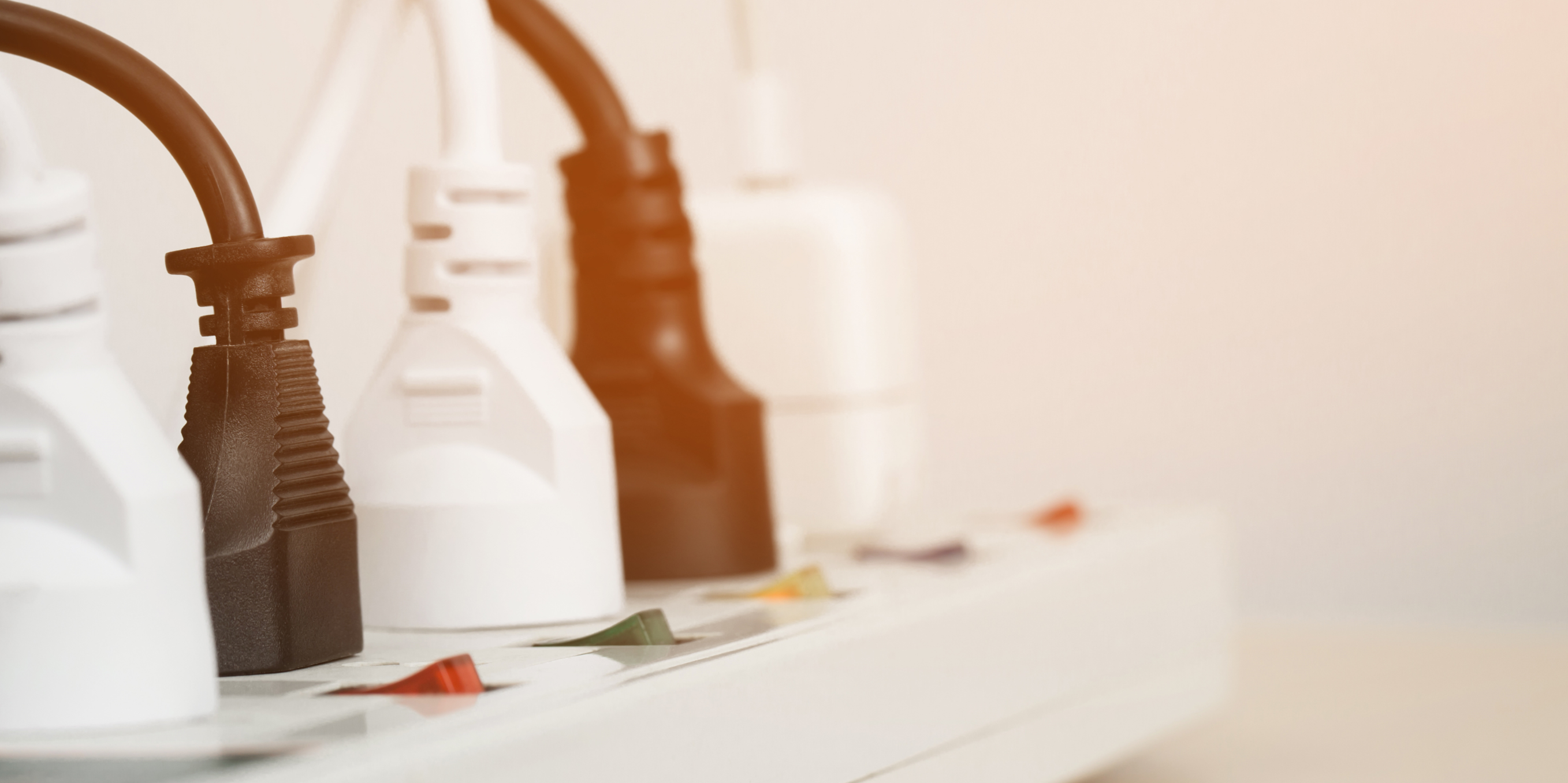 A row of electrical cords plugged into a power outlet. The power strip has four outlets, and each outlet is plugged into an electrical cord. The cords are different colors and lengths.